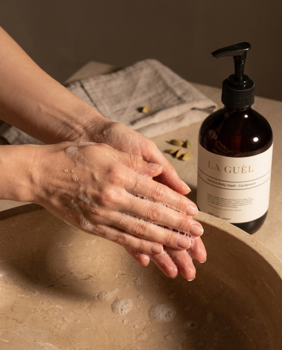 Dłonie w delikatnej pianie mydła La Guèl, naturalny manicure, obok bursztynowa butelka.